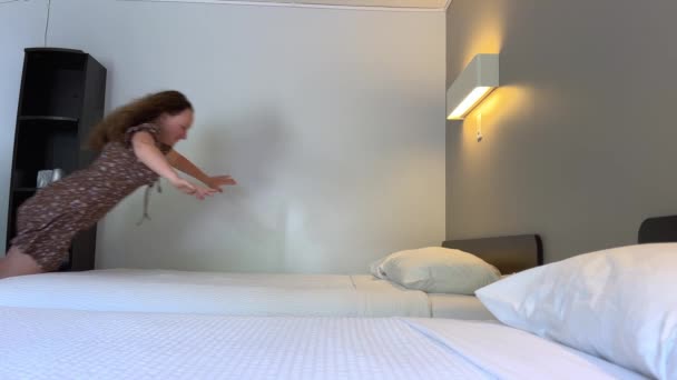 一个年轻的少女在一家旅馆里跳着白雪公主的床去休息旅行放松秋天的休息枕头手挥动着腿穿着运动鞋在空中飞舞棕色的衣服 — 图库视频影像