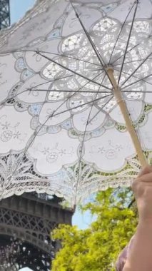 Neşeli bir genç kız Eyfel Kulesi 'nin arka planında duruyor. Elini kaldırdı. Paris' e seyahat acentesinin reklamını yapabilirsiniz. Kızlar bir açık iş şemsiyesinin ellerinde