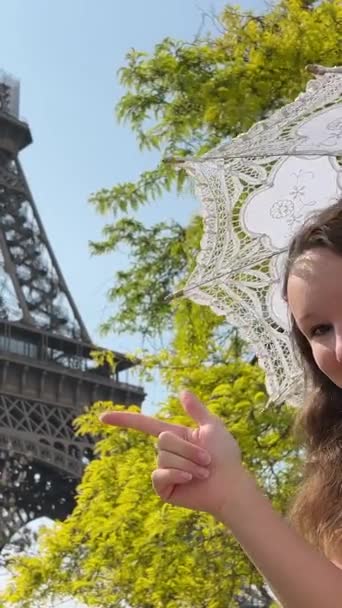 エッフェル塔を背景に傾いているフレームを見て美しい10代の少女彼女は笑顔とパリへの旅行のためにここに偉大な広告を示しているようだ 高品質ビデオ — ストック動画