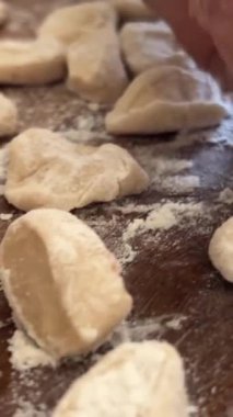 Yaşlı bir kadının yaşlı elleri hamuru yuvarlar ve bir şeyler pişirir ya da hamur köftelerini ya da hamur köftelerini ahşap bir yüzeyde kaynatır. Yüksek kalite 4k görüntü