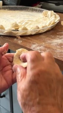 Mavi bluzlu ve beyaz atkılı bir büyükanne torunları için turta ve diğer hamurları pişirir.