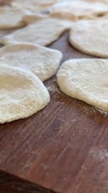 Büyükannem torunu için lezzetli börekler, turtalar ya da börekler hazırlar. Hamuru sallar, parçalara ayırır ve masanın üzerinde heykeller yapar. Üzerinde un serpiştirilmiş hamurlar vardır.