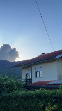 Dağlarda kırmızı çatılı beyaz bir ev dağın tepesindeki büyük bir buluta karşı güneş bulutun önünü aydınlatıyor. Yüksek kalite 4k görüntü