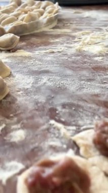  Hamur köftelerini heykeller ve ahşap bir masaya koyar, onlardan bir sürü vardır, unu iştah açıcıdırlar ve pişirilmeyi beklerler her hamur köftesi etle doludur, yuvarlaktır ve düzgünce el yapımıdır.