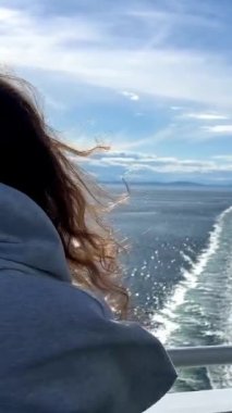 Genç kız yolcu gemisiyle uzaklaşıyor. Uzağa bakıyor. Giyinmiş, denizde feribot ayak izleri var..