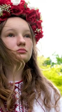 Güzel, cesur Ukraynalı, kırmızı çelenkli, saçları örgülü yeşil ağaçların arkasında duran, nakış işlemeli gömlekli, güçlü, cesur genç bir kadın.