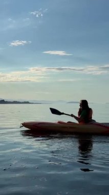 a teenage girl is kayaking at sunset in the Pacific Ocean, only the silhouette of Kayak and Paddles is visible she swims along a sunny path to the sea. a beautiful sky with small clouds