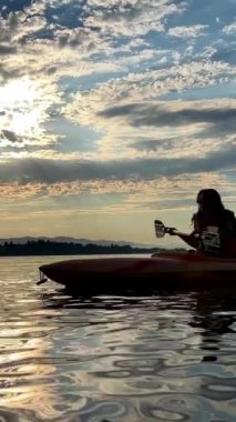 a teenage girl is kayaking at sunset in the Pacific Ocean, only the silhouette of Kayak and Paddles is visible she swims along a sunny path to the sea. a beautiful sky with small clouds