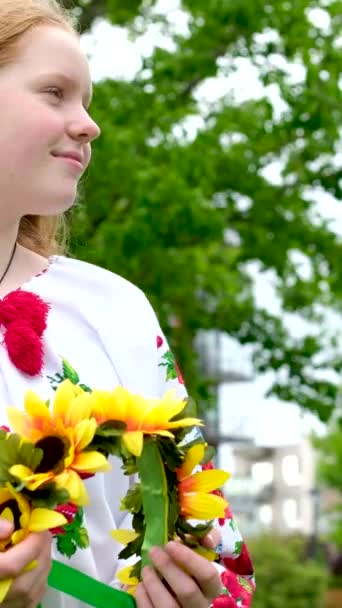 鮮やかな赤い髪をした日当たりの良い女の子は 平和のためにウクライナの女性の刺繍の民族シャツの花輪と緑の木の背景に立っていますウクライナの愛国心の勝利はありません — ストック動画