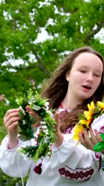 2美しいウクライナの女の子織り花輪刺繍シャツ緑の自然は近くに家に座っていますウクライナのエンターテイメントパーティーで休息通信歌を歌う国家儀式笑顔トーク — ストック動画