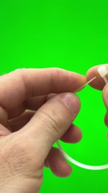 On a green background, a chromakey man fastens a nylon tie with his own hands. He pulls the long end through the hole and secures it nylon tie