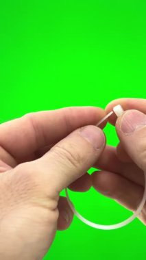 On a green background, a chromakey man fastens a nylon tie with his own hands. He pulls the long end through the hole and secures it nylon tie