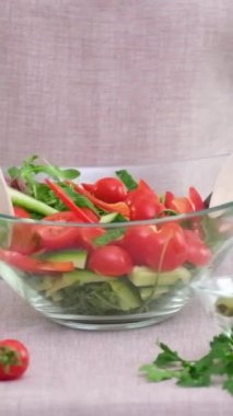 Tahta kaşıklarla yoğurulan salata, kiraz domatesleri, salatalıklar, zeytin salatalıkları bej masa örtüsü bej önlüklü diğer malzemeler masada yatıyor. 