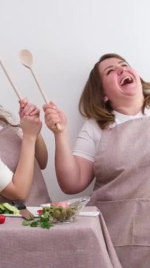 Afiş 2 neşeli sinsi şefler ahşap kaşıklarla salata hazırlıyorlar genç ve orta yaşlı kadınları aynı şekilde giydiriyorlar domates için. 