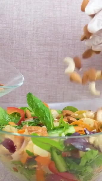 在新鲜沙拉中添加坚果素食杏仁榛子腰果许多配料绿色蔬菜妇女在白色手套和米黄色围裙特写 — 图库视频影像