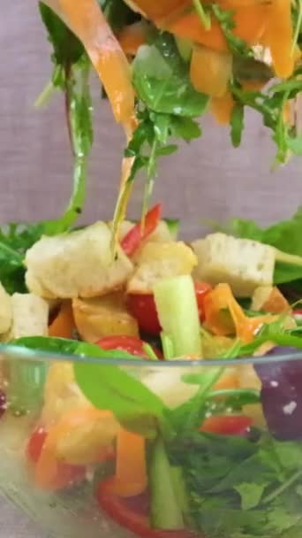 女性が野菜サラダの具材をボウルに入れて混ぜる クローズアップベジタリアンサラダの具材を混ぜ合わせる野菜サラダの準備 スローモーションビデオ落下レタスをガラス板ニンジンに混ぜて — ストック動画