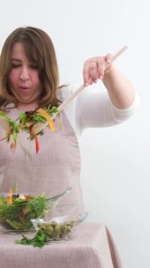 woman eating salad at table with organic vegetables, enjoying healthy diet, standing in light kitchen interior. Lady cooked veggie meal at home. Weight loss concept. High quality photo