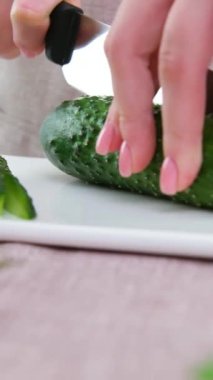 Healthy eating dieting concept. High angle view of female hands cutting cucumber in kitchen right side tomatoes sliced lettuce on left cucumbers white porcelain board gentle manicure young female hand