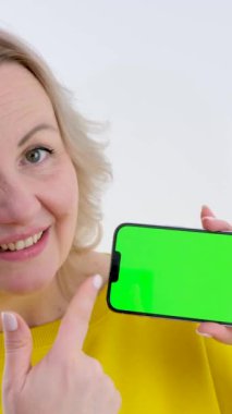 Telefonu olan güzel bir kadın. Yeşil arka plan krom anahtarı. Gülümseyen bir parmak.