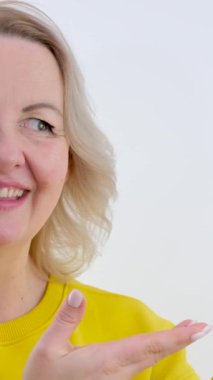 Sarı elbiseli kadın parmaklarıyla reklam programınız için boş bir arkaplanı işaret ediyor. Elleriyle gülümseyerek dans ediyor. Gözleri güldürüyor.