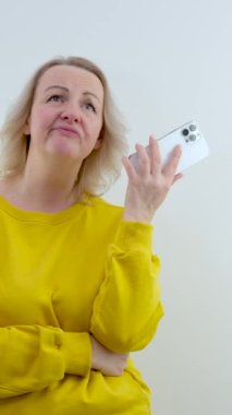 Ellerinde telefonuyla tatminsiz üzgün bir kadın dudaklarını kabarttı ve turuncu sarısı bir arka planda üzgün duruyor. 