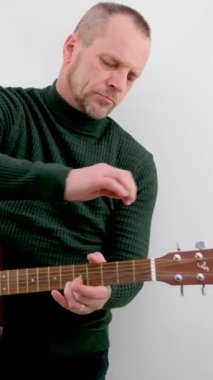 Bir adam gitar çalan bir müzisyenin gitar ve erkek ellerini yakından akustik gitar çalarken ayarlıyor. Müzik beyaz arka plan Yeşil kazak reklamı