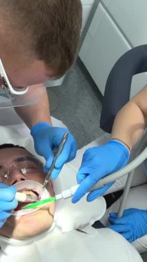 Mavi eldivenli doktor, hastaların dişlerine, temizlenmesi gereken plağın nerede olduğunu gösteren bir merhem sürüyor. Dişçi Ukrayna Vinnitsa 26.12.2022 kliniğinde diş temizliği ve cilalama yaptırıyor.