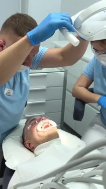 Diş hekiminde dişçi hasta asistanı. Hastanede bir erkek hastayı tedavi eden diş hekimleri Kıyamet Günü Diş Temizleme Doktoru ve asistanı Ukrayna Vinnitsa Diş Hekimliği 12.2022