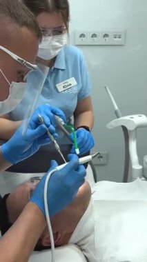 Diş hekiminde dişçi hasta asistanı. Hastanede bir erkek hastayı tedavi eden diş hekimleri Kıyamet Günü Diş Temizleme Doktoru ve asistanı Ukrayna Vinnitsa Diş Hekimliği 12.2022
