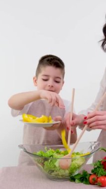 Mutfakta Anne ve Şirin Küçük Çocuk Sağlıklı Yemek Yapıyor. Ebeveynler küçük oğluna sağlıklı alışkanlıkları ve sebzeleri salata kasesinde nasıl karıştıracağını öğretiyor. Sevimli Çocuk Ailesine Yardım Ediyor