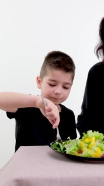 Masa başında siyah elbiseli anne oğul anneyi sebze salatasıyla besliyor anne babaya çatal yemeyi öğretiyor çocuklarla iletişim kurmaktan zevk alıyor. 