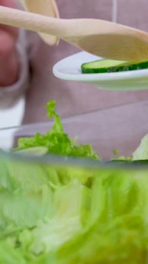 Professional female cook adding fresh cucumber slices in glass bowl with salad. mother and child preparing vegetable salad close-up boys hands help mother to add cucumbers glass plate