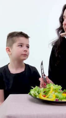 Siyah gömlekli ve siyah önlüklü güzel bir kadın, oğluna temiz mutfakta süs olsun diye sahte meyve ve sebze düzenlemeyi öğretiyor. Yüksek kalite 4k görüntü