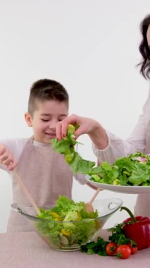 Anne oğlu taze sebze salatası pişiriyor. Çocuk, iki tahta kaşıkla yemek yapıyor. Evet, marul yaprakları serpiştiriyor. 