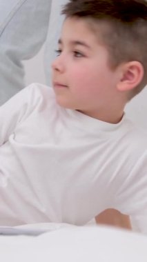 4-6 yaşlarında bir çocuk annesiyle yatağa yatar. Yanına uzanır ve tablet üzerinde çalışır. 