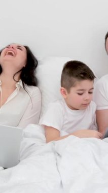 Yatakta, tabletle oynayan bir aile. İçtenlikle gülüyorlar. Anne ve baba ve oğul. 