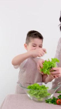 Anne oğul salatayı elleriyle hazırlıyor marul yaprakları beyaz arka planda çocuklara lezzetli sağlıklı yemek yapmayı sebze vitaminlerini vejetaryenlik yararına kullanmayı öğretiyor.