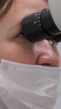 Bayan doktorun yakın plan yüzü mikroskopla mikroskoba bakar maske protezleri üzerinde rahatça nefes alır mikroskop teknolojisiyle kanalları doldurur. 