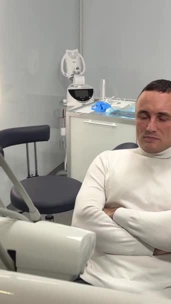 一个英俊的男人坐在牙科诊所的一个牙座上 全身都穿着白毛衣 — 图库视频影像