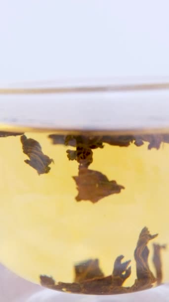 お湯で渦巻く大きな葉のガラスの中に紅茶をダブルボトムで淹れるグラスカップ垂直ビデオ — ストック動画
