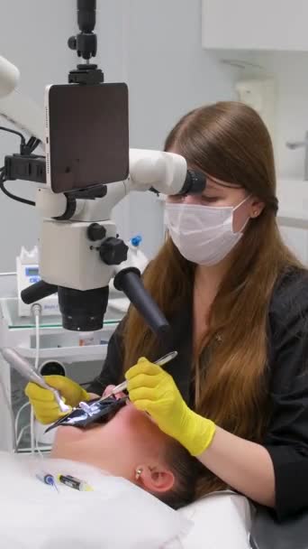 歯科医院最新機器と技術女性医師は テキストのための大きなタブレット画面の白い背景スペースを持つ顕微鏡を使用して患者の歯を扱います — ストック動画