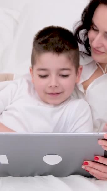 妈妈的儿子舒服地躺在床上放松漂亮的酒店玩着游戏平板电脑打回家去了另一个国家的白衣黑头发爱照顾母亲 — 图库视频影像