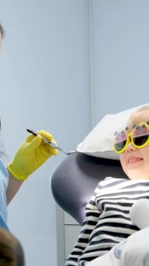 Pediatrik diş hekimliği. Sarı eldivenli güzel doktor ışığı açıyor. Kıza diş bakımı için kullanılan aletleri gösteriyor. 