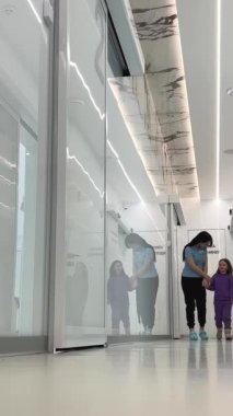Kadın ve kız koridor boyunca yürür birbirlerine bakarlar büyük beyaz koridor şeffaf beyaz kapı yansıması hastane bakım konsepti çocuklara yardımcı olur.
