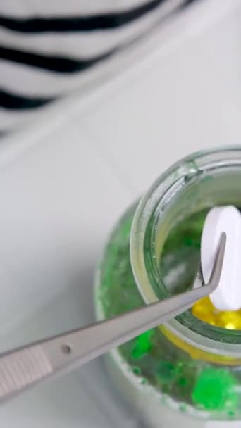 Używanie Szczypiec Zrzucania Dużej Białej Pigułki Butelki Zielonym Płynem Złotem — Wideo stockowe