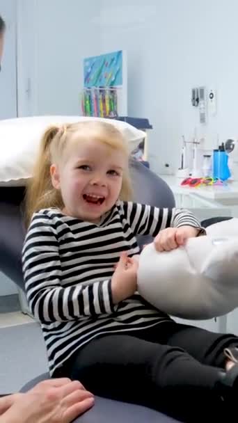 小さな女の子の歯医者を示す若い医者歯科医への最初の旅行幸せな笑顔楽しい会話ミルク歯治療看護師フェアヘアの女の子の子供 — ストック動画