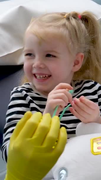 医生展示小女孩牙科椅子第一次去牙医那里快乐的微笑愉快的谈话乳牙治疗护士金发碧眼的女婴牙科 — 图库视频影像