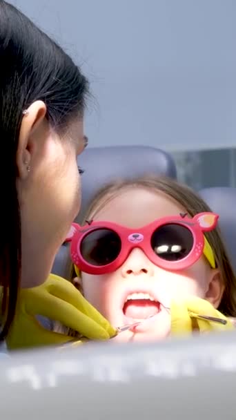 小児科クローズアップ小さな女の子オープン口ショー歯医者見ますかどうか彼女持っていますケア充填治療検査によって医師の女の子身に着けています — ストック動画