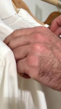 Erkeklerin kıllı elleri, ahşap askılık konsept mağazasındaki beyaz kıyafetleri yavaş yavaş ayırıyor. Kıyafet sıklığı kısırlığı.