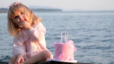 Pembe elbiseli küçük bir kız oturur ve pembe bir pasta yer. Güzel bir okyanus denizinin zemininde üç mum ve bir kalemle. Şirin suratlar.